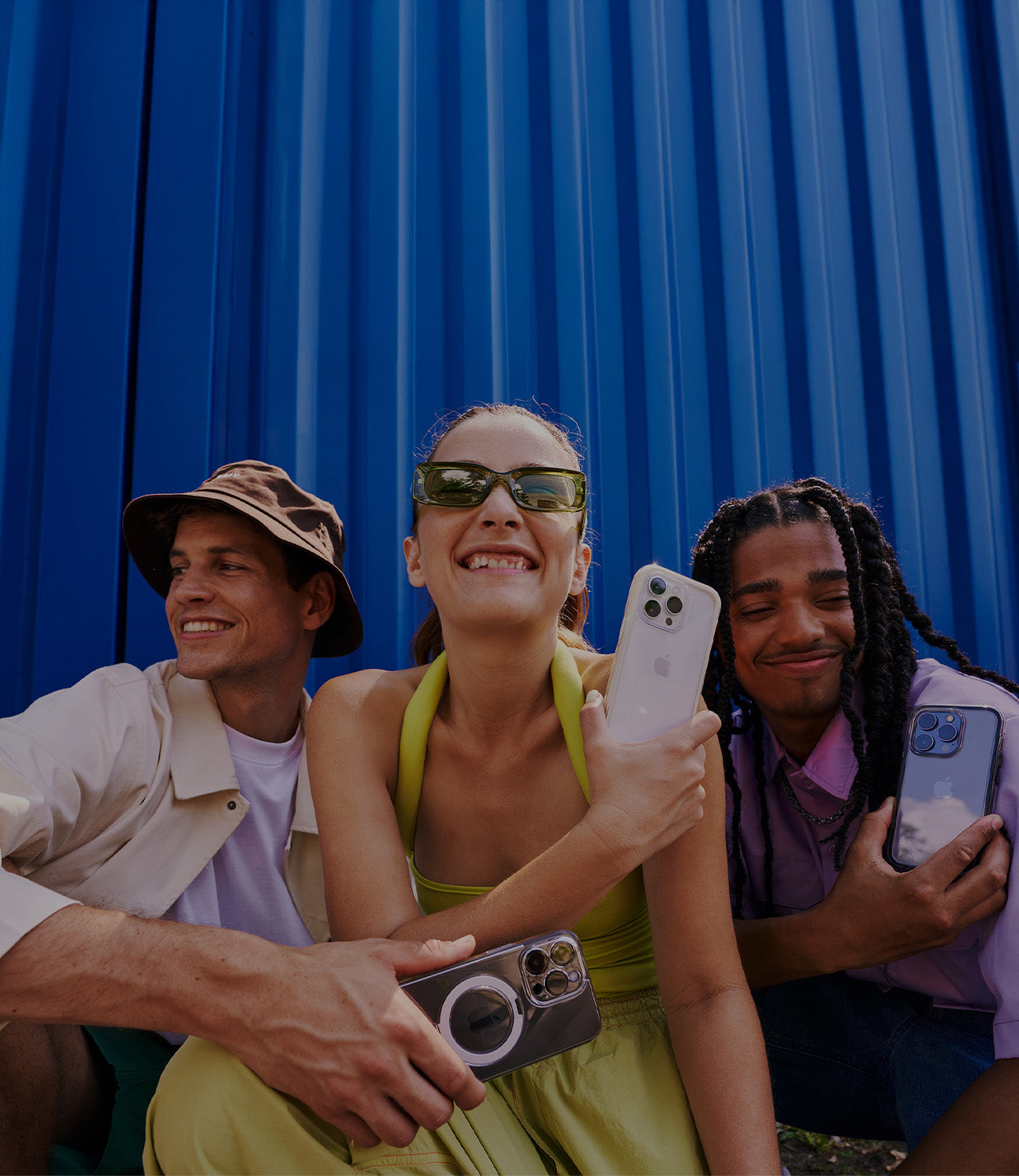 Three friends smiling and holding stylish phone cases, posing against a vibrant blue background, showcasing modern and trendy designs